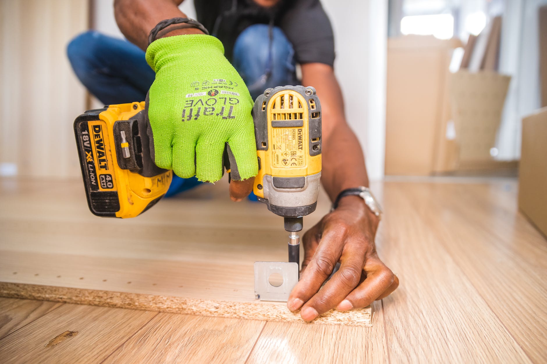 A person is using a cordless drill to attach a bracket to a piece of wood lying on the floor.