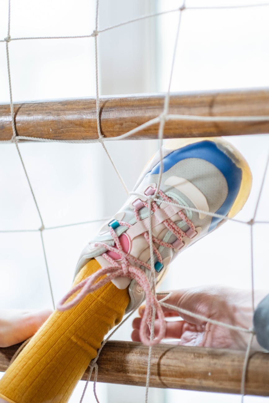 A persons' leg and running shoe are stuck in in a net and hands appear to be trying to help untangle them.